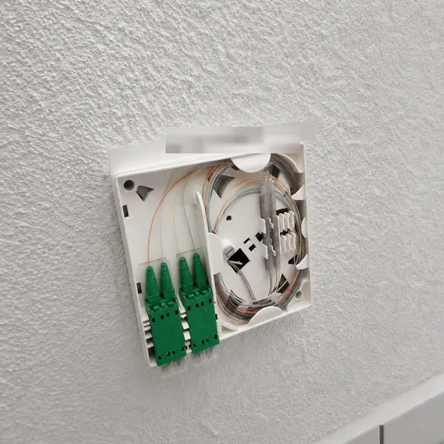 Prise fibre optique OTO ouverte avec connecteurs verts SC/APC et fibre lovée, posée sur un mur intérieur